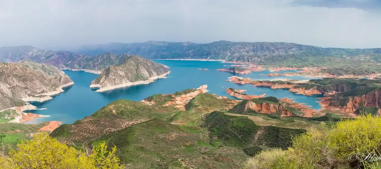 The blue waters of the Nurek reservoir among green and red hills