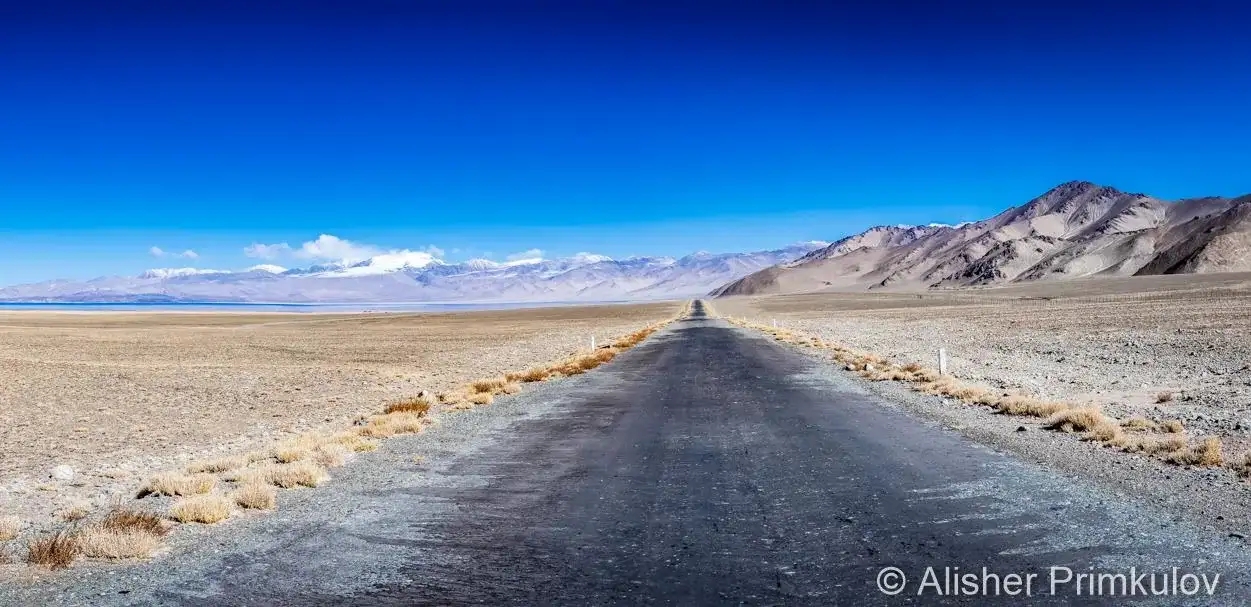 The empty Pamir Highway M41 running straight across a high desert plain