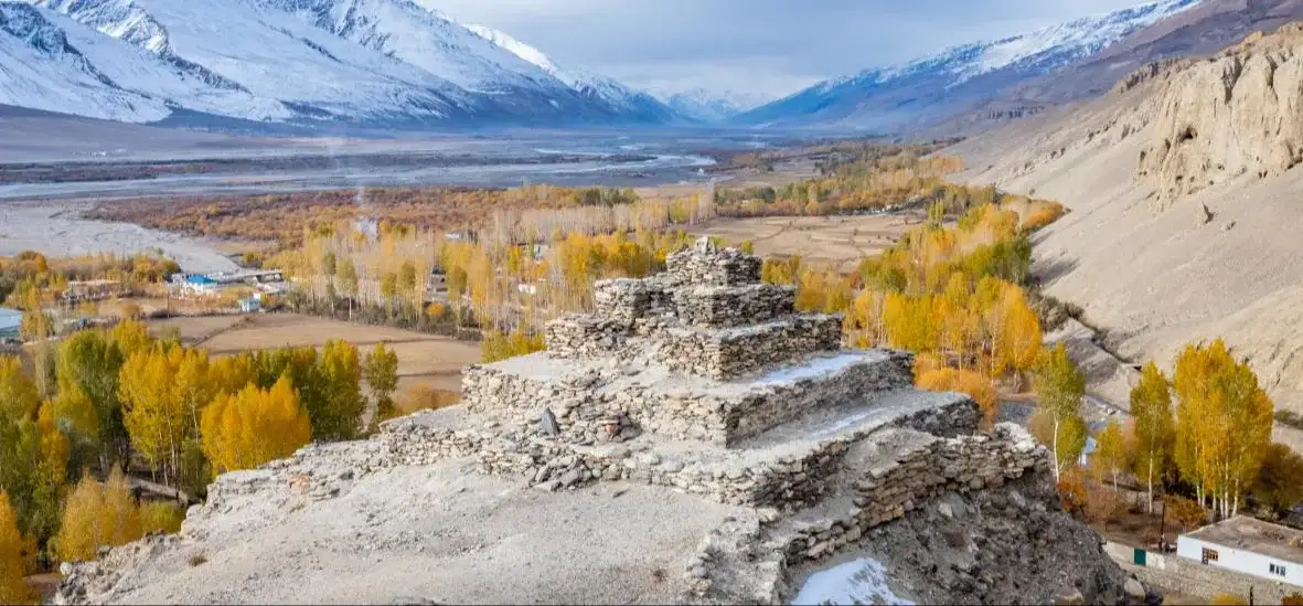 Autumn trees and fortress ruins in the Wakhan valley below snowy peaks